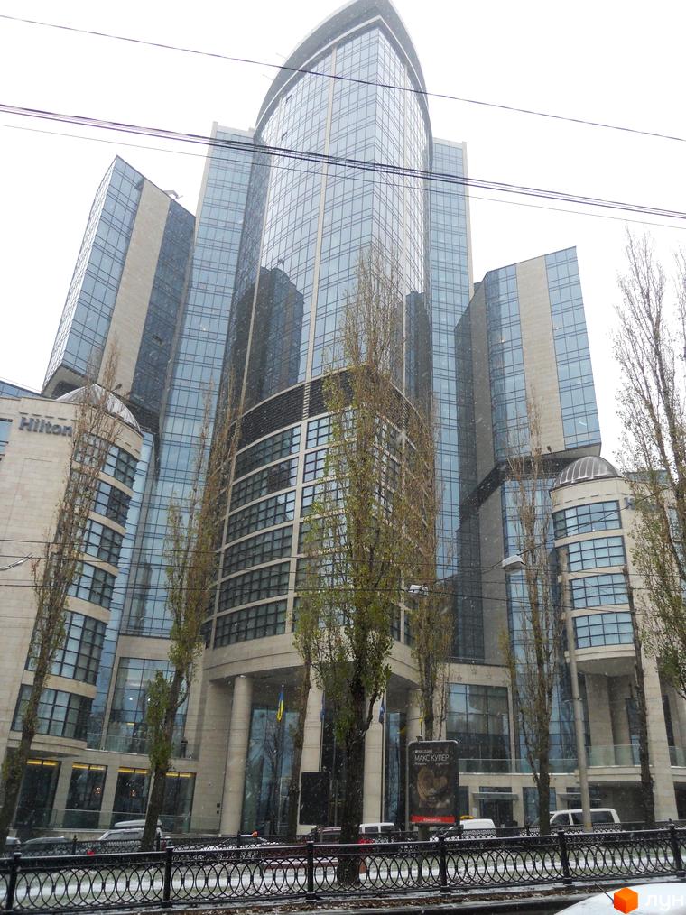 Житловий комплекс H-Tower з сучасною фасадною облицюванням та прибудинковою територією з деревами та паркувальними місцями.