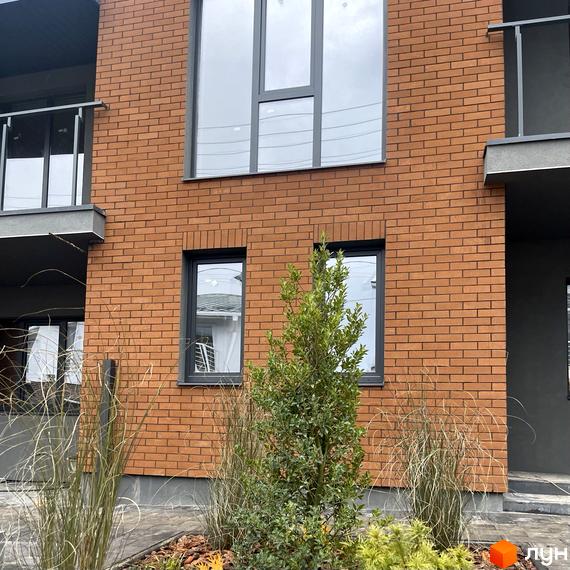 Фасад будинку КМ Панич 3.0 з цегляним оздобленням та великими вікнами. На прибудинковій території зелені насадження та декоративні трави.