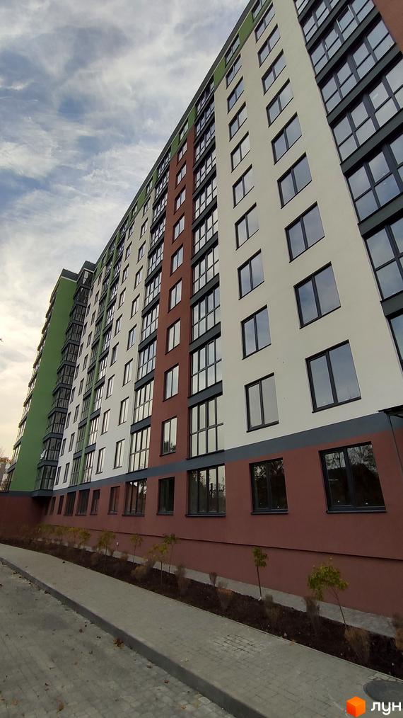 Зовнішній вигляд багатоповерхового житлового комплексу на вулиці 600-річчя з фасадами білого, коричневого та зеленого кольорів. Прибудинкова територія з бруківкою та висадженими деревами.