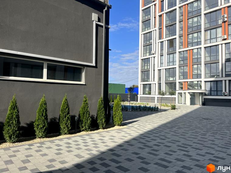 Житловий комплекс City Line: багатоповерховий будинок з великими вікнами та помаранчевими елементами. Двір вимощений плиткою, присутні зелені насадження.
