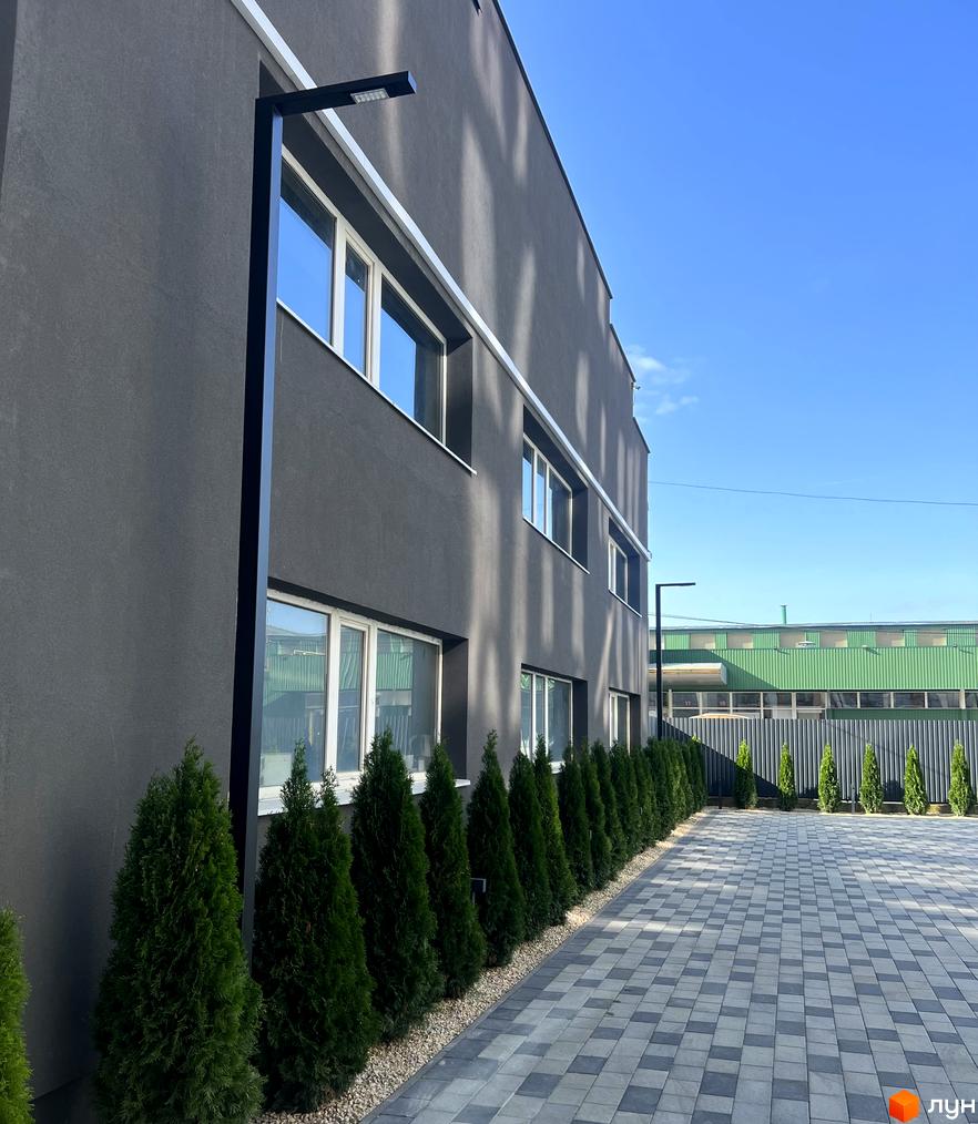 Темно-сіра будівля житлового комплексу City Line з білими вікнами та чорними ліхтарями. Прибудинкова територія має ряд зелених туй та вимощену плиткою доріжку.