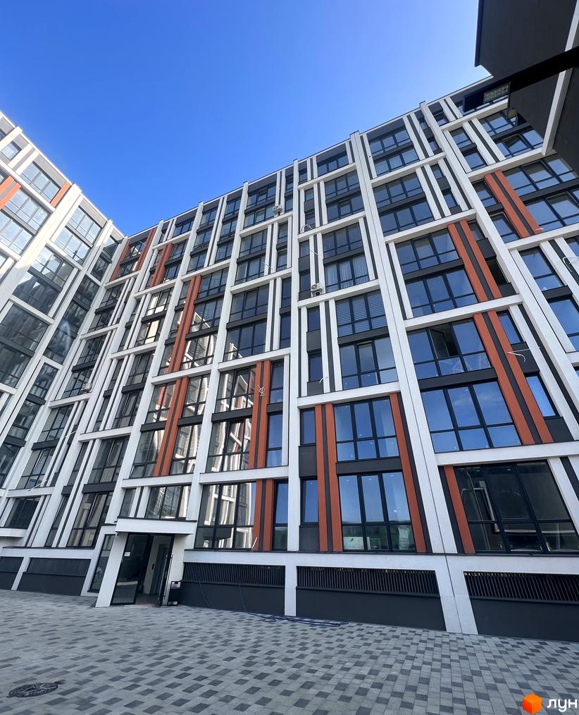 Зображення фасаду житлового комплексу City Line з великими вікнами та кольоровими вставками. Вигляд на внутрішній двір з тротуарною плиткою.