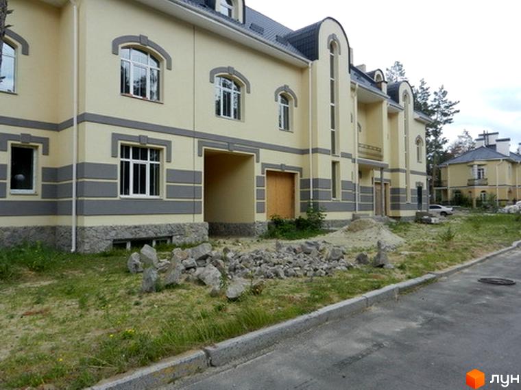 Зовнішній вигляд житлового комплексу КМ Сосновий бір з жовтою фасадною обробкою та прибудинковою територією з камінням.