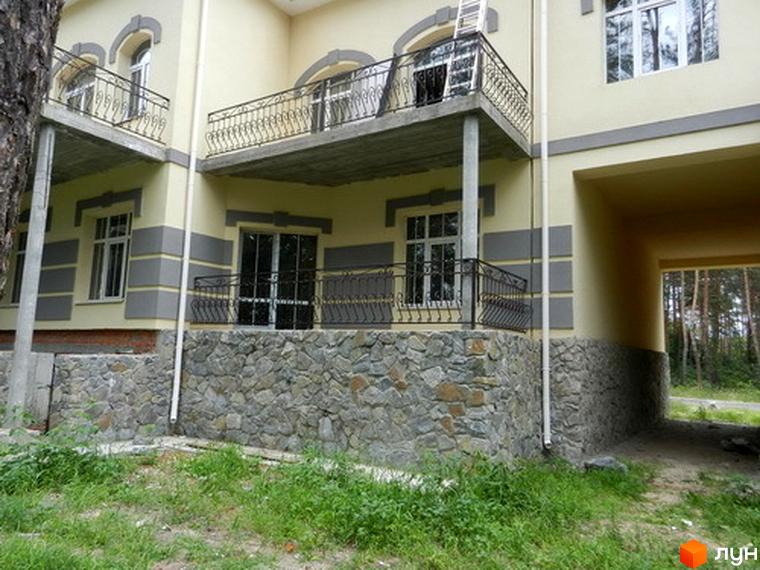 Зовнішній вигляд будинку в Котеджному містечку Сосновий бір з балконами та кам'яним оздобленням. Навколо будинку зелена прибудинкова територія.