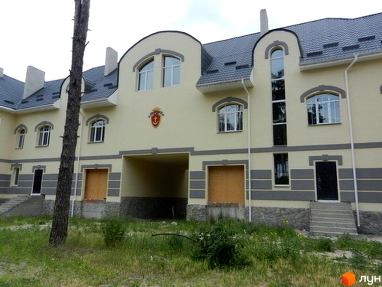 Зображення фасаду Котеджне містечко Сосновий бір. Двоповерховий будинок з сірим дахом та світлим фасадом, перед будинком зелена трава.