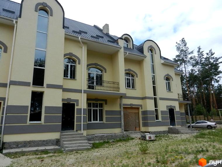 Зовнішній вигляд Котеджного містечка Сосновий бір: триповерховий будинок з великими вікнами та сірим дахом. Навколо будинку зелена трава та дерева.