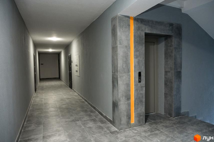 Коридор в новобудові ЖК Сонячна Долина з сірими стінами, плиткою на підлозі та дверима. Поруч розташований ліфт.