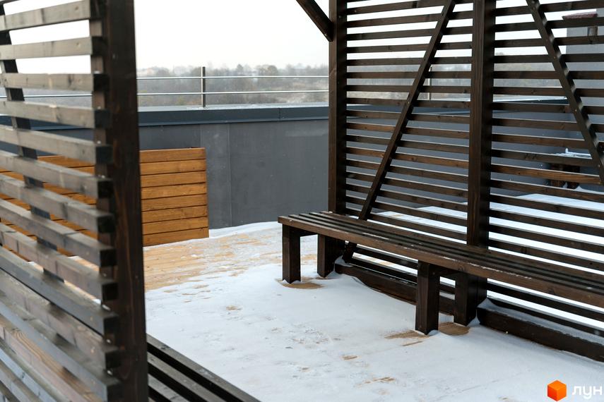 Зимовий вигляд тераси Житлового комплексу Сонячна Долина з дерев'яною перголою та лавкою, вкритою снігом.