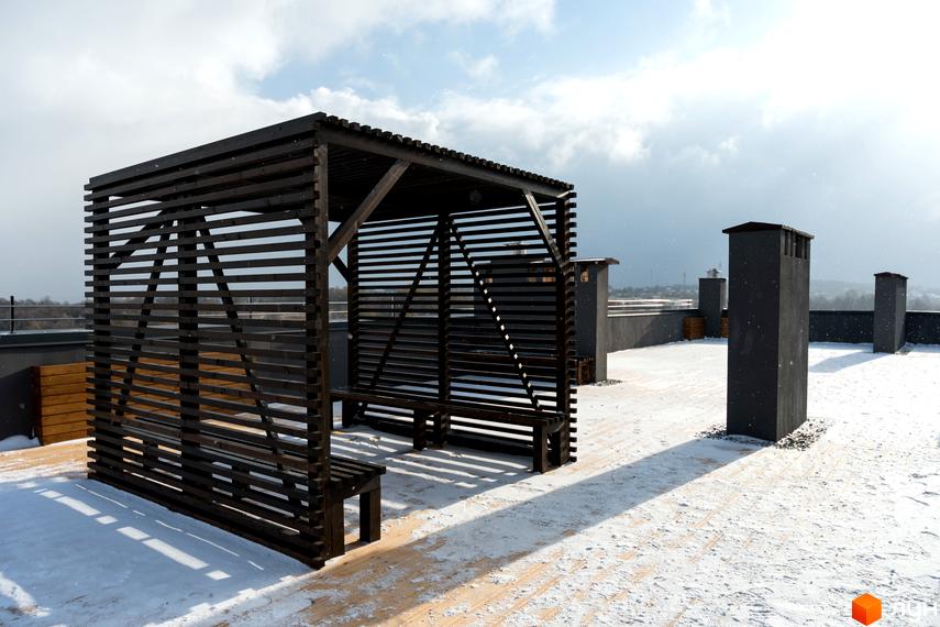 Дах Житлового комплексу Сонячна Долина взимку, з дерев'яною перголою, лавками та димоходами на засніженій терасі.