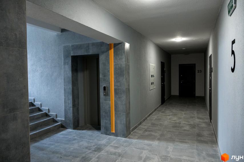 Внутрішній простір під'їзду Житлового комплексу Сонячна Долина: сірі стіни, плиткова підлога, ліфт з помаранчевою смугою та сходи.