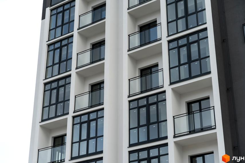 Житловий комплекс Сонячна Долина: багатоповерховий будинок з білим фасадом, великими вікнами у темних рамах та балконами зі скляними огорожами.