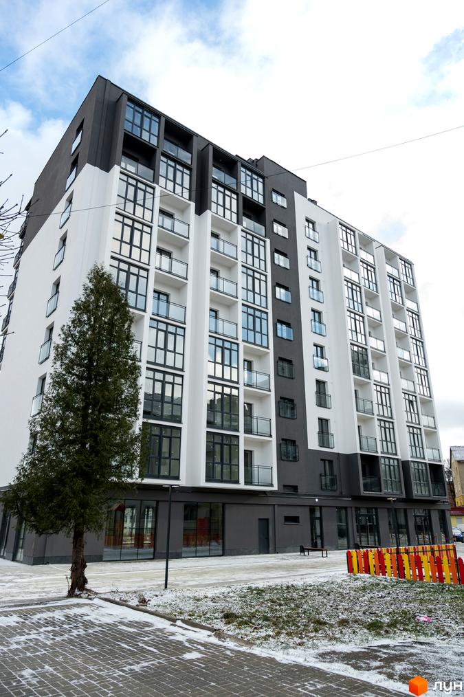 Будинок Житлового комплексу Сонячна Долина з білими та темно-сірими фасадами. Прибудинкова територія з бруківкою, деревом та кольоровим парканом.