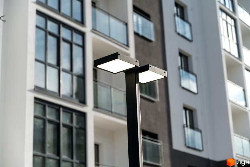 Житловий комплекс Сонячна Долина з білим та сірим фасадом, великими вікнами та балконами. Поруч стоїть вуличний ліхтар.