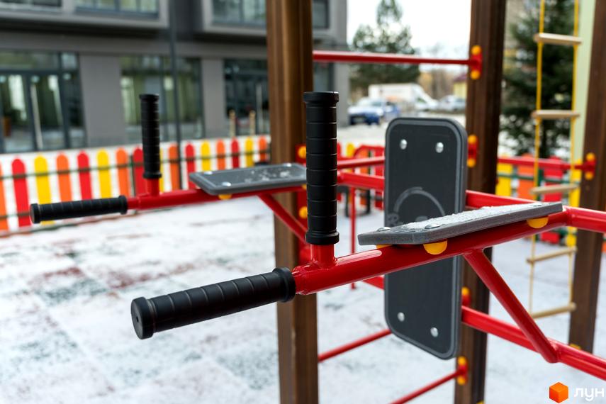 Фасад будинку Житлового комплексу Сонячна Долина та спортивний майданчик з червоними тренажерами на засніженій території.