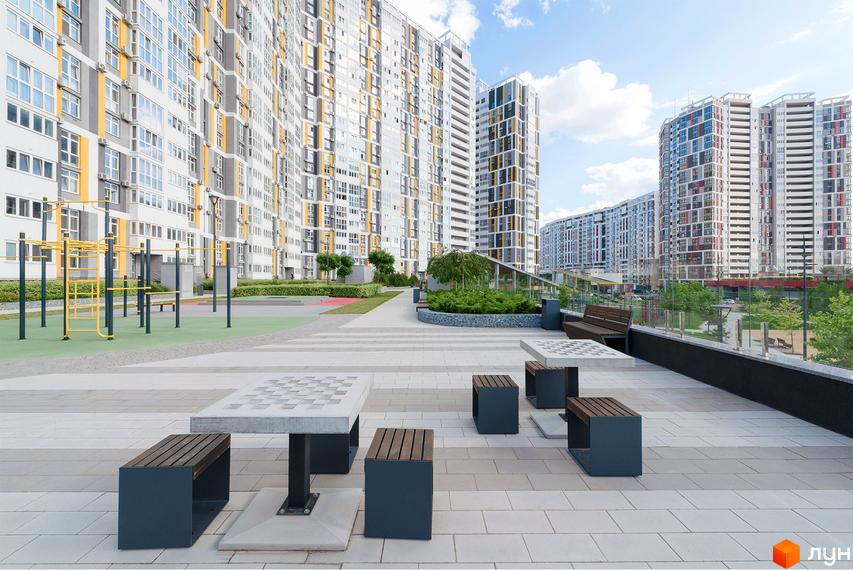 Житловий комплекс Русанівська Гавань: висотні будинки з біло-сірими та жовтими фасадами. На території є зони відпочинку, ігрові столи та спортмайданчик.