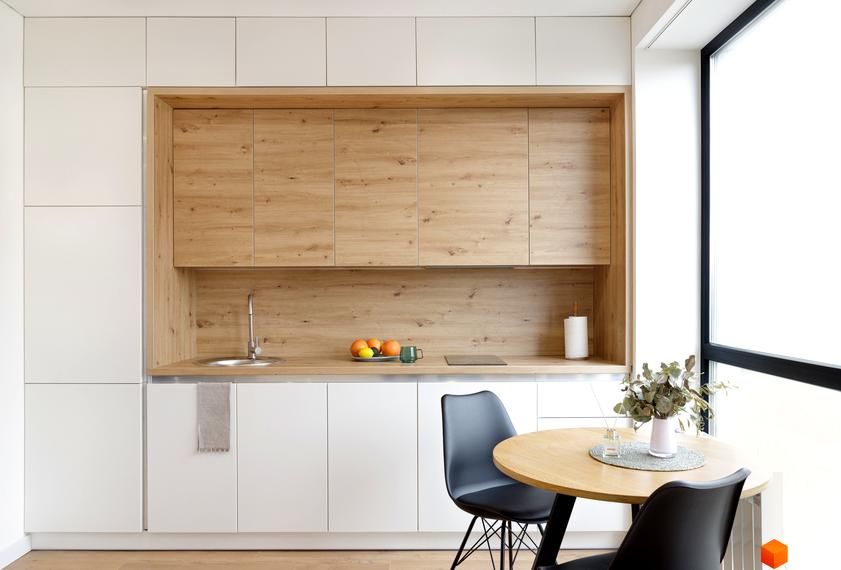 Сучасна кухня з дерев'яними фасадами та білими шафами, обідній стіл з двома стільцями біля вікна в житловому комплексі Coliving ONE Nivki.