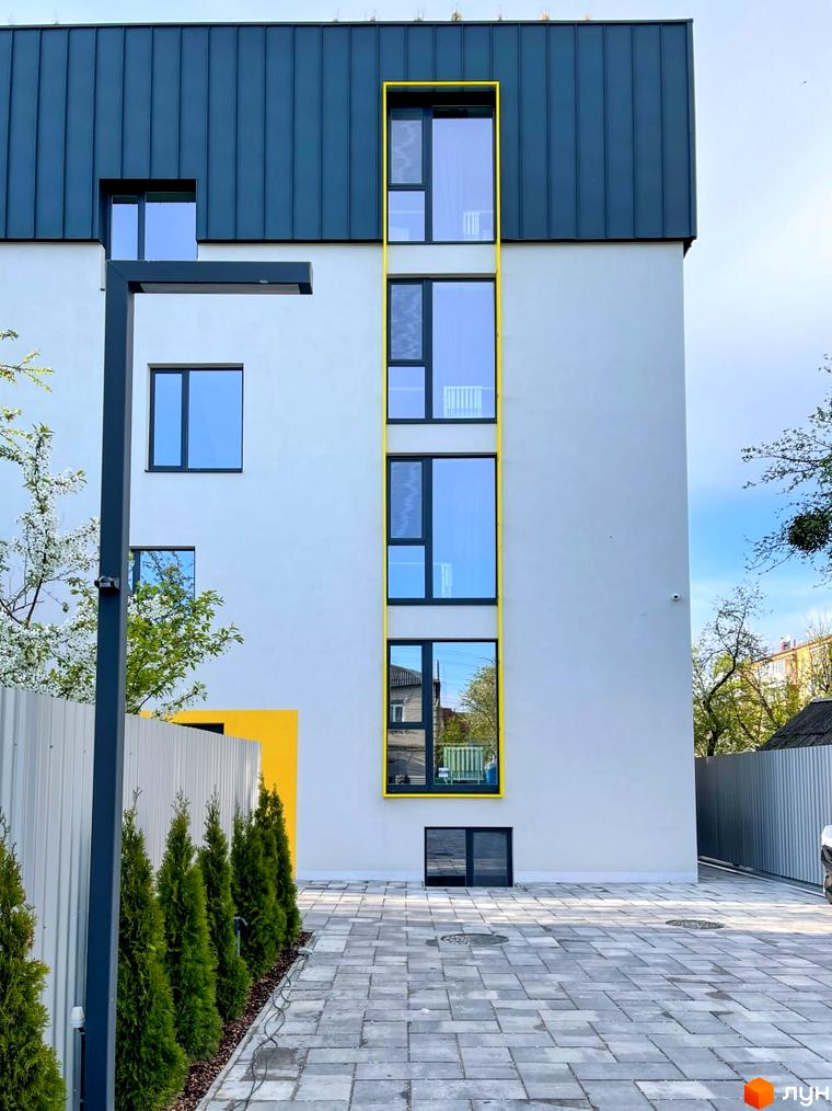 Зовнішній вигляд будинку житлового комплексу Coliving ONE Nivki з вікнами та фасадом, прибудинкова територія з деревами та бруківкою.