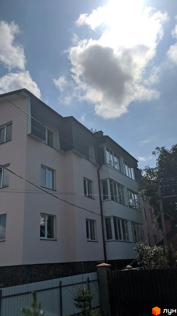 Зовнішній вигляд будинку по вул. Наварійській, 29д. Фасад світло-бежевого кольору, дах темний, багато вікон та балконів. Навколо будинку паркан та зелені насадження.