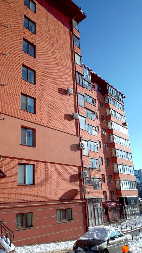 Зовнішній вигляд цегляного житлового комплексу на вулиці Березова, 4а, з кондиціонерами та вікнами. Навколо видно засніжену територію та припаркований автомобіль.