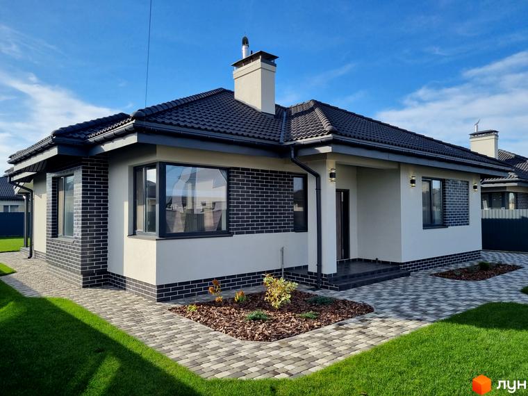 Котеджне містечко КМ Сонячний: одноповерховий будинок з темною черепицею та цегляним фасадом, доглянута прибудинкова територія з газоном та бруківкою.