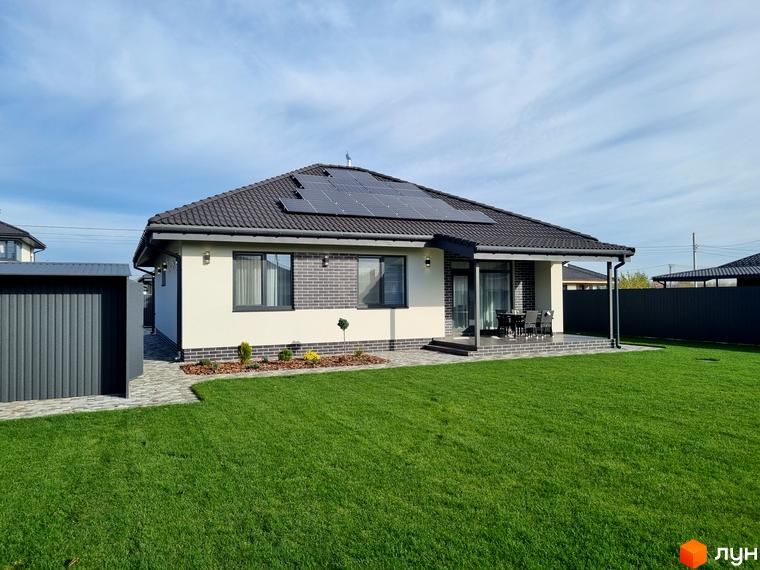 Котеджне містечко Сонячний: одноповерховий будинок з сонячними панелями на даху та доглянутою зеленою ділянкою. Навколо будинку бруківка та зелений газон.