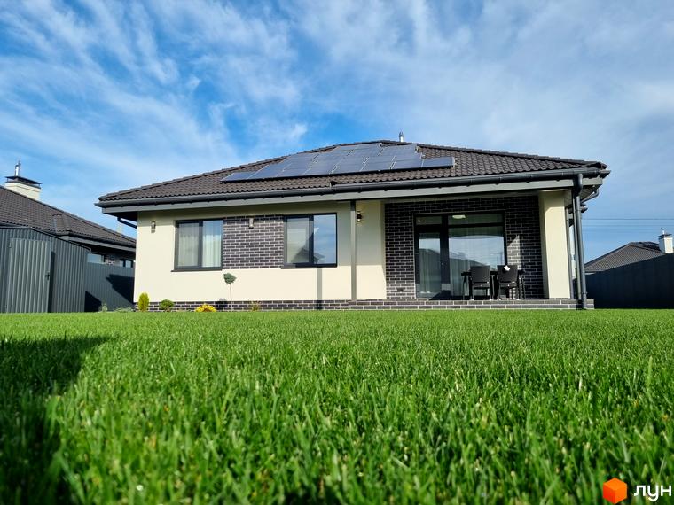 Котеджне містечко КМ Сонячний: одноповерховий будинок з сонячними панелями на даху та зеленою галявиною перед ним. Сучасний дизайн фасаду з цегляними елементами.