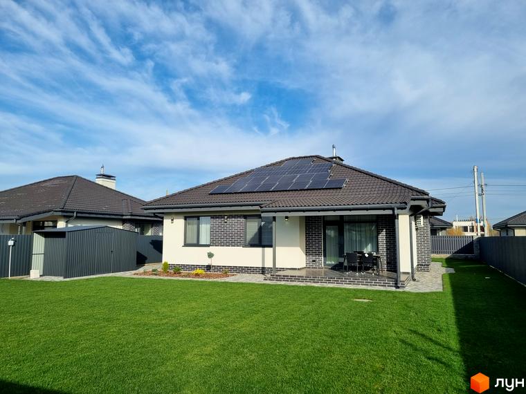 Котеджне містечко Сонячний: одноповерховий будинок з сонячними панелями на даху, цегляним фасадом та зеленою галявиною. Навколо будинку розташована доглянута прибудинкова територія з доріжками та огорожею.