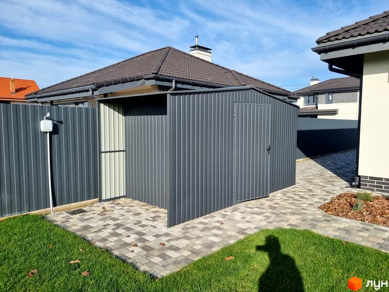 Котеджне містечко КМ Сонячний: сірий металевий сарайчик та доріжка з плитки на прибудинковій території. Зелена галявина з травою.