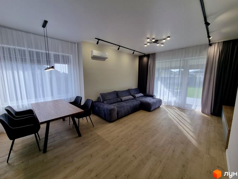 Вітальня з обідньою зоною в Котеджному містечку Сонячний. Простора кімната з диваном, столом та стільцями біля великих вікон з білими шторами.