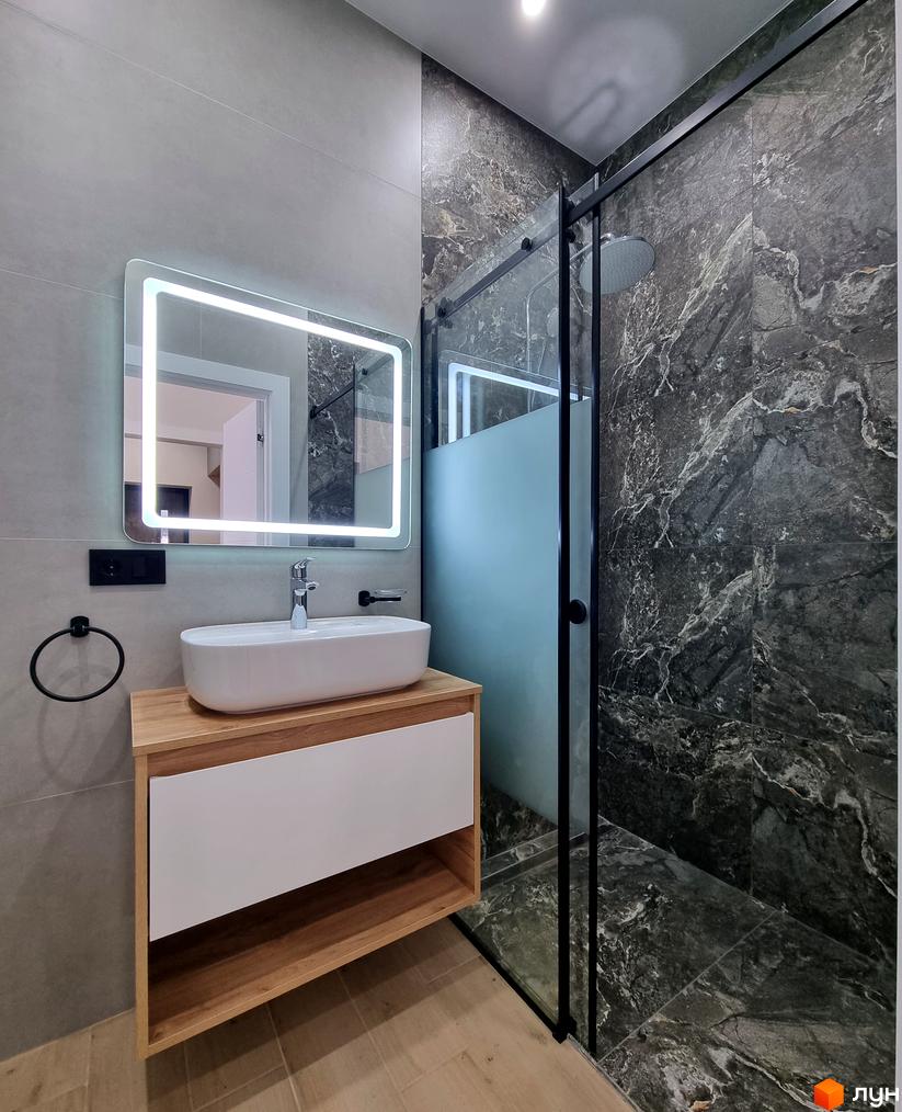 Сучасний дизайн ванної кімнати в КМ Сонячний з мармуровим оздобленням та підсвіченим дзеркалом. Оцініть деталі інтер'єру новобудови.
