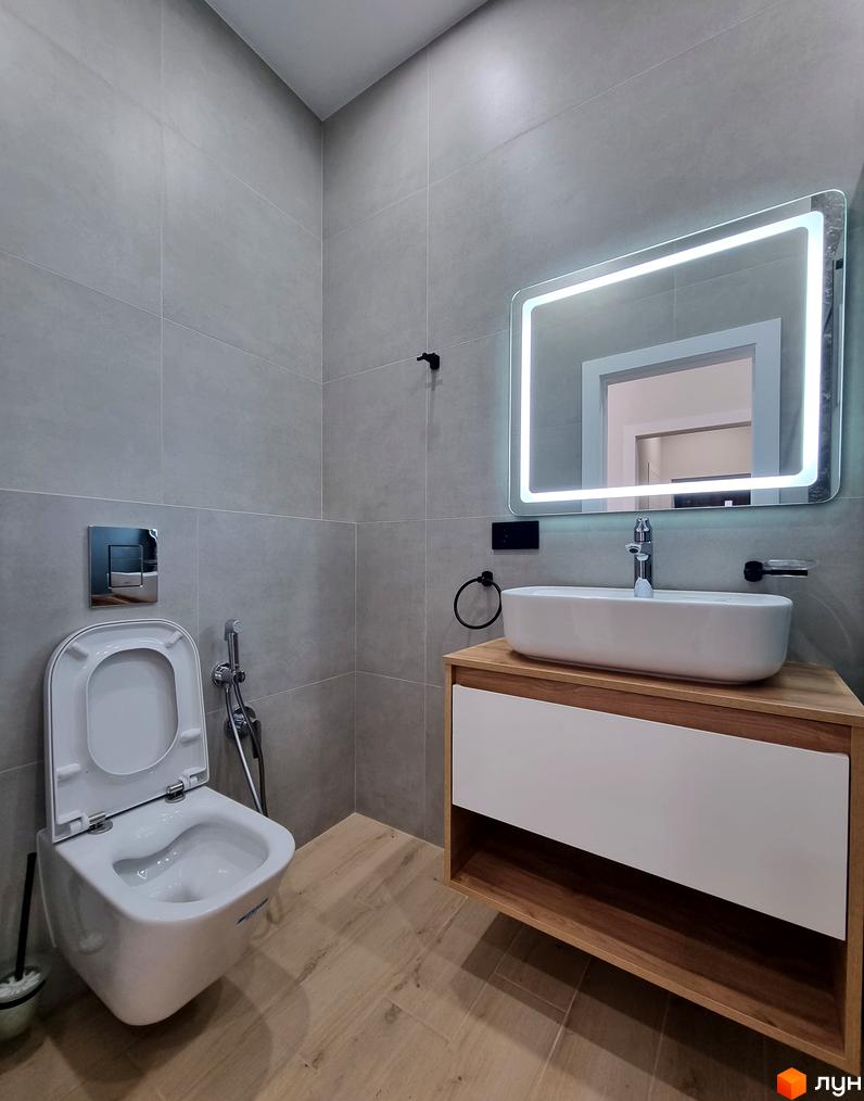 Сучасний дизайн ванної кімнати в новобудові КМ Сонячний з підвісним унітазом та тумбою під раковину. Сіра плитка та дерев'яні елементи створюють затишну атмосферу.