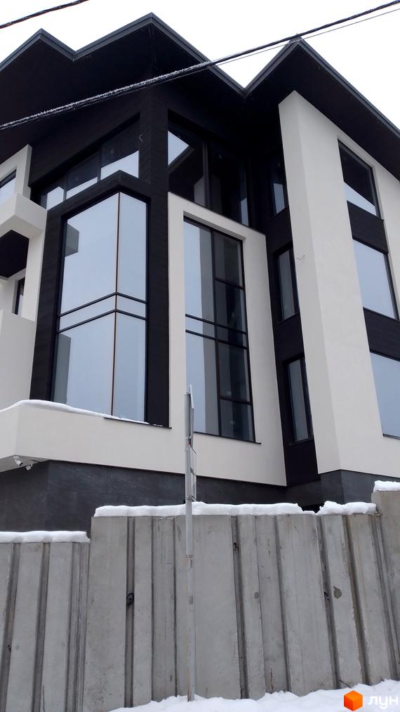 Зовнішній вигляд новобудови на вул. Урожайна з великими вікнами та чорно-білим фасадом. На передньому плані бетонний паркан та сніг.