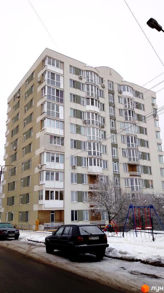 Зовнішній вигляд багатоповерхового житлового комплексу на вулиці Золотогірській. Поруч розташований дитячий майданчик та припарковані автомобілі.