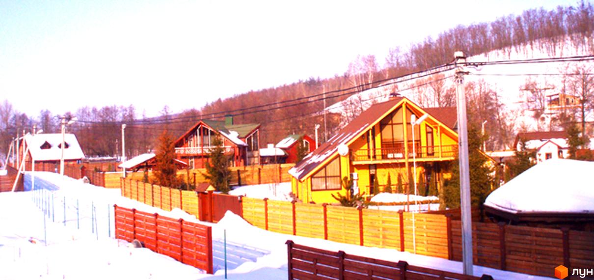 Котеджне містечко Заріччя. Зимовий пейзаж з будинками з похилими дахами, дерев'яними парканами та засніженими ділянками. На задньому плані видно ліс.