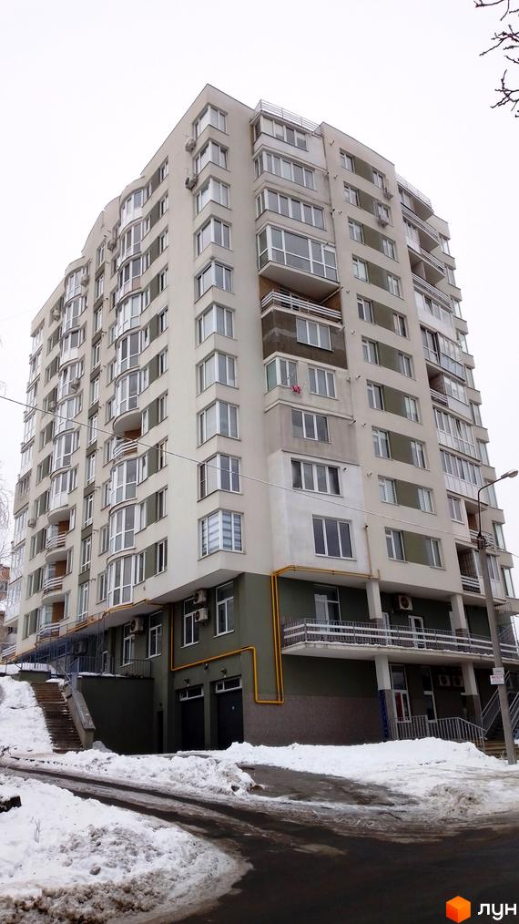 Зовнішній вигляд багатоповерхового житлового комплексу на вулиці Золотогірській. Навколо будинку видно засніжену прибудинкову територію та дорогу.