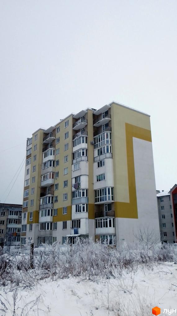 Зовнішній вигляд житлового комплексу на вулиці Золотогірська, 14а, з фасадом жовтого та білого кольорів та балконами. Навколо комплексу видно засніжену територію з деревами.