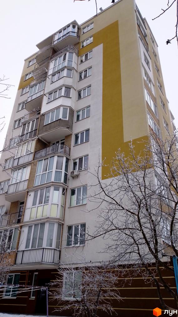 Фасад багатоповерхового житлового комплексу на вулиці Золотогірська, 14а, з балконами та заскленими лоджіями. Навколо видно гілки дерев, вкриті інеєм.