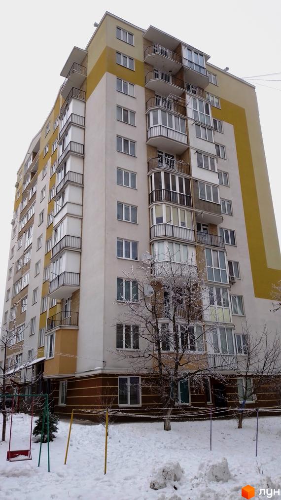 Зовнішній вигляд новобудови на вул. Золотогірська, 14а, з балконами та вікнами, на тлі сніжної прибудинкової території з гойдалкою.