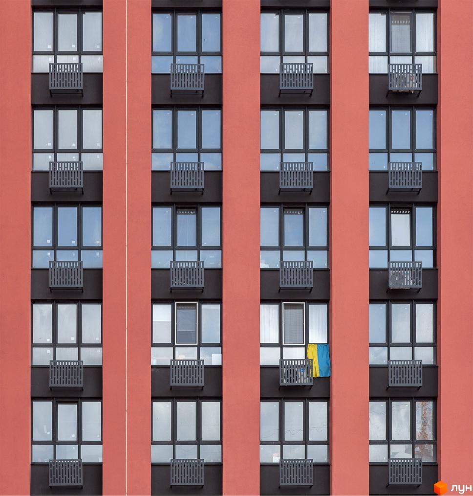 Фасад DOCK32 з червоно-коричневими стінами та темними віконними рамами, обладнаний декоративними металевими балконами. Видно український прапор.