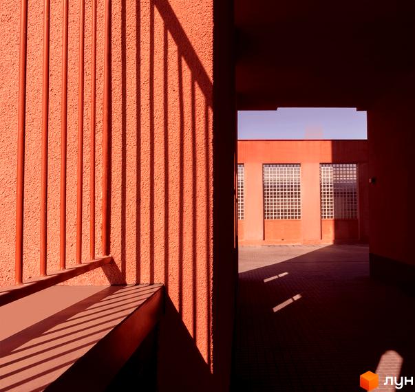 Будівля житлового комплексу DOCK32 з теракотовим фасадом та великими вікнами. На подвір'ї видно тіні від огорожі.