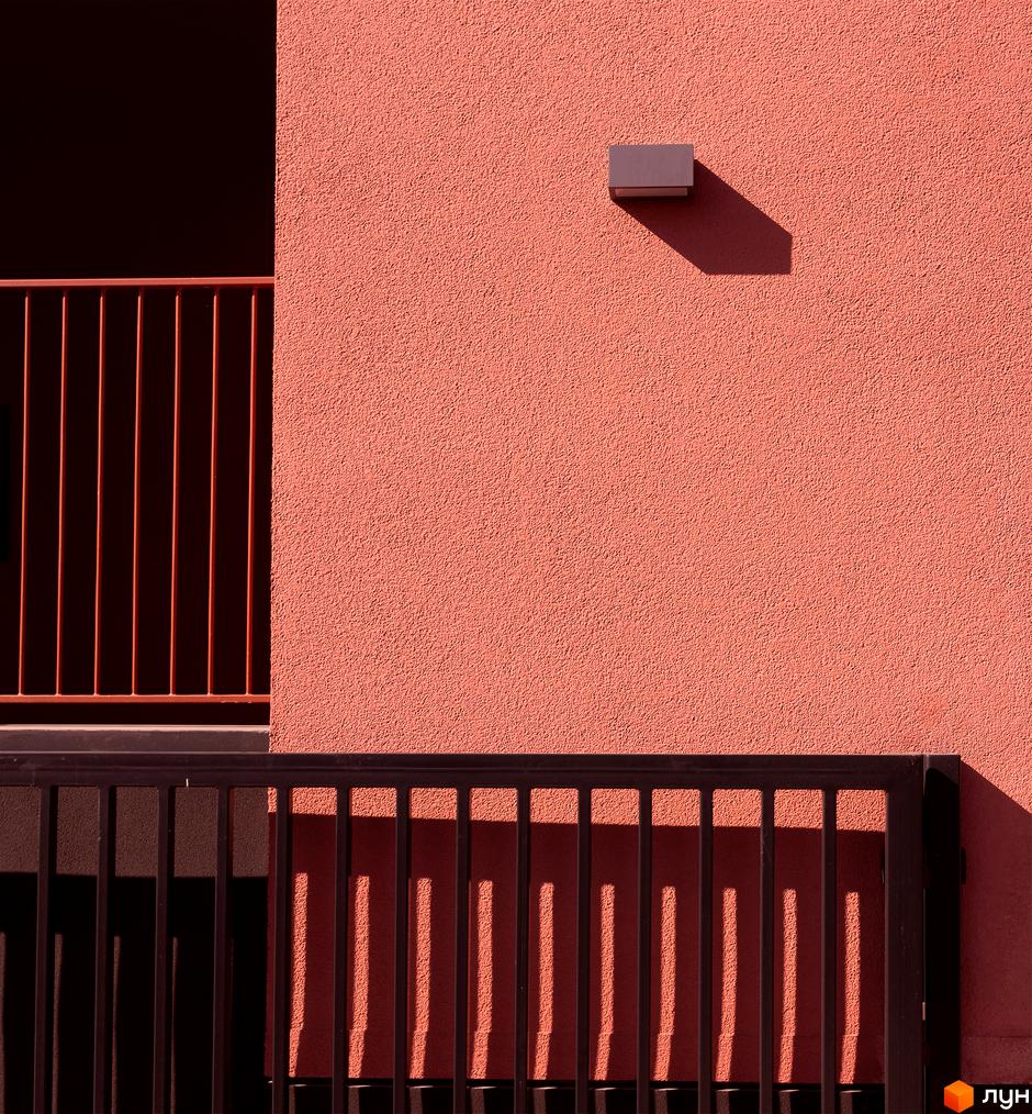Фасад житлового комплексу DOCK32 з текстурованою теракотовою стіною, ліхтарем та перилами, що відкидають чіткі тіні.
