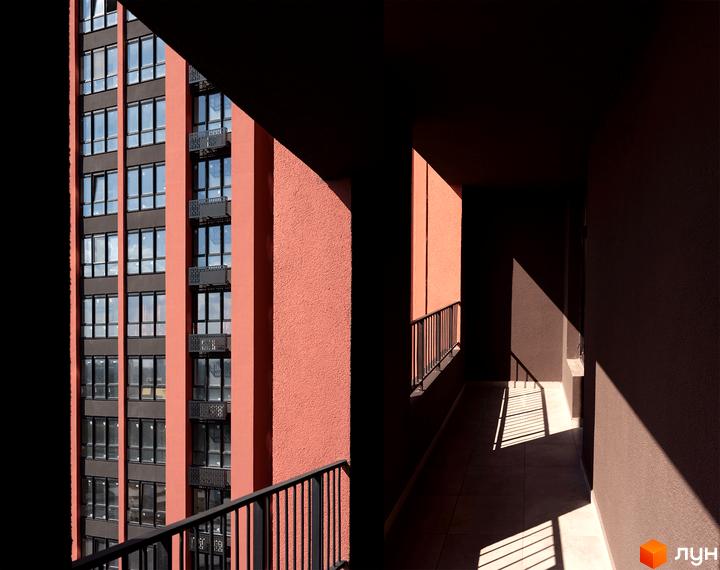 Високий будинок DOCK32 з теракотовим фасадом та темними віконними рамами. На передньому плані балкон з металевими поручнями та сонячними променями на підлозі.