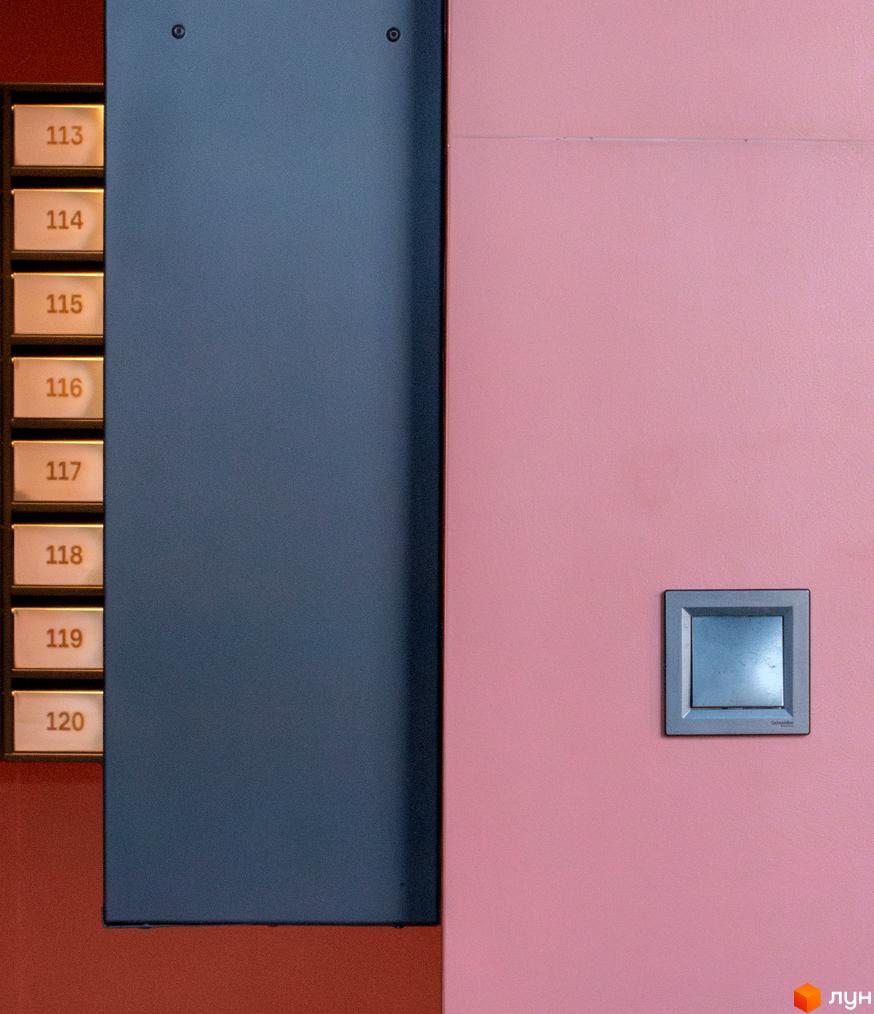 Інтер'єр житлового комплексу DOCK32: стіна з номерами квартир 113-120, темно-сіра панель та рожева стіна з блоком керування.