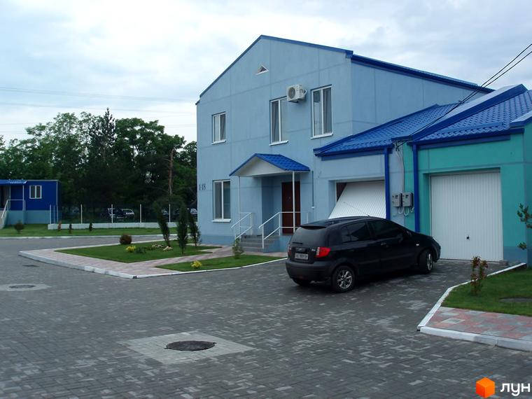 Зовнішній вигляд будинку житлового комплексу КМ Блакитне озеро з блакитними стінами та дахом. Прибудинкова територія з зеленими насадженнями та асфальтованою парковкою.
