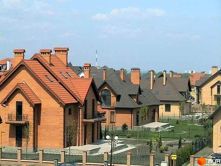 Зовнішній вигляд котеджного комплексу КМ Олана з червоною черепицею та прибудинковою територією з зеленими насадженнями.