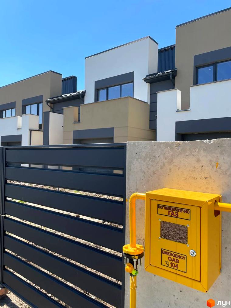 Зовнішній вигляд таунхаусів Vlasne 1 з сірими та білими фасадами, на тлі блакитного неба. На прибудинковій території видно огорожу та газовий бокс.