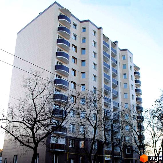 Зображення багатоповерхового будинку на вулиці Любецька, 2а. Вигляд фасаду з балконами та вікнами, навколо дерева.