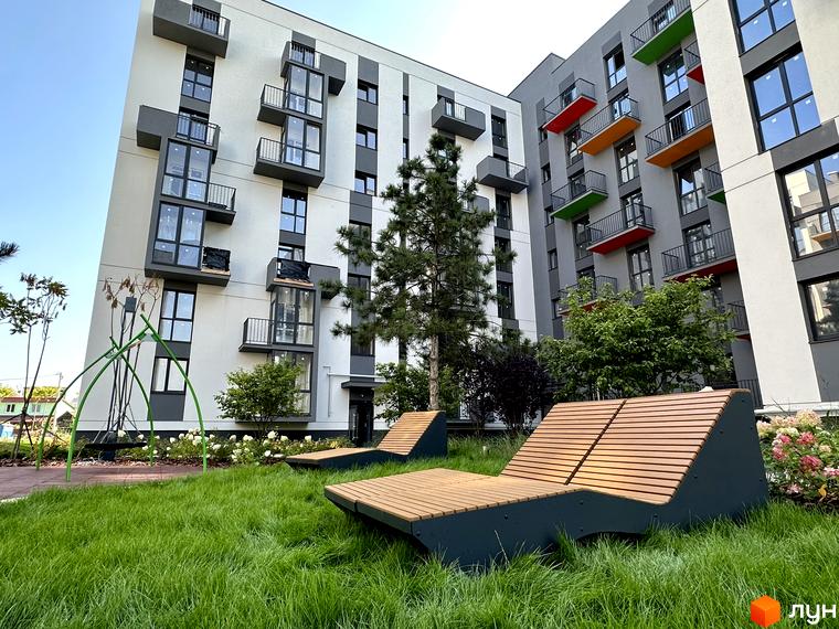 Зображення житлового комплексу Проект Панорама з білими та сірими фасадами. На території зелена трава та лаунж-зони для відпочинку.
