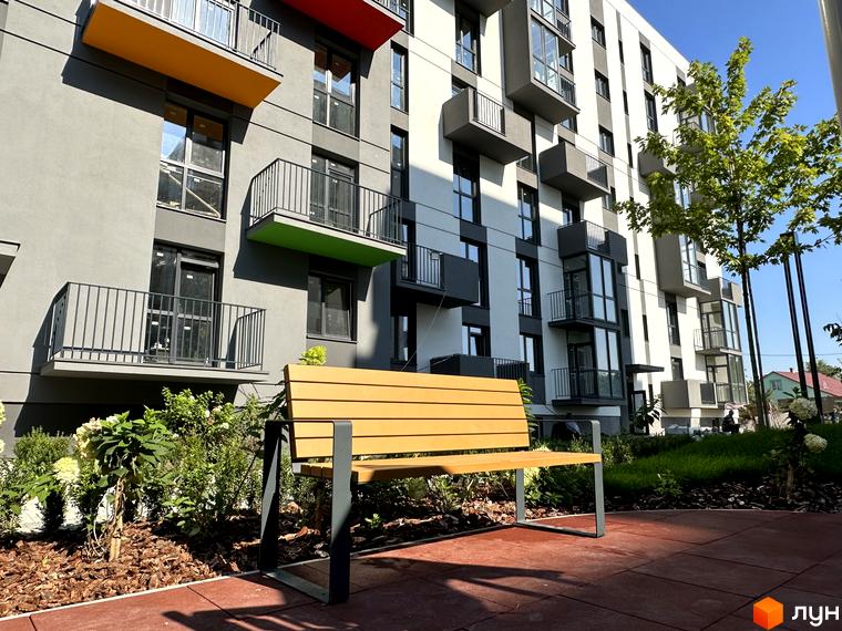 Житловий комплекс Проект Панорама з яскравими балконами та зеленою прибудинковою територією з лавкою.