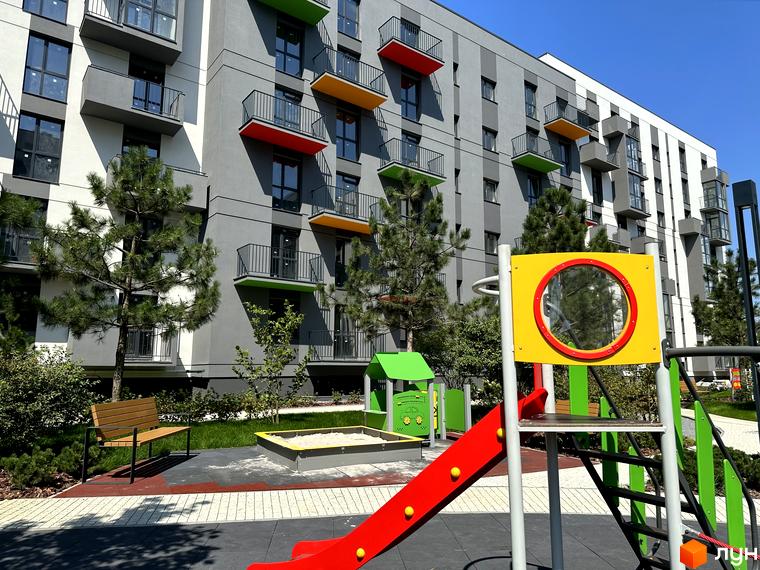Зображення фасаду багатоповерхового будинку ЖК Проект Панорама з кольоровими балконами та дитячим майданчиком на прибудинковій території.